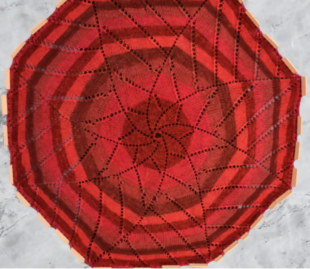 A Close up of an octagonal shaped blanket in alternating shades of red from the outside in. There's a star flower-like pattern within it.